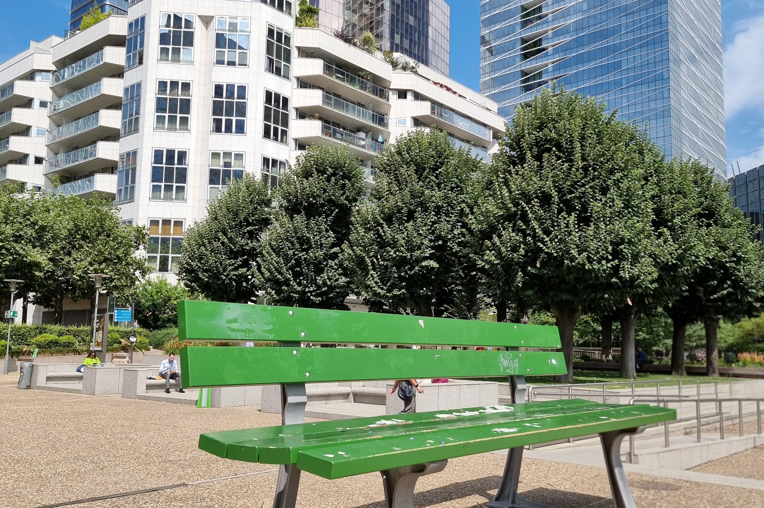 Banc vert dans un parc parisien contemporain bordé d’immeubles récents